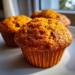 Close-up of three moist pumpkin muffins on a white plate, baked to a golden brown.