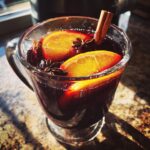 A close-up of a glass mug filled with warm mulled wine, garnished with orange slices, star anise, and a cinnamon stick.