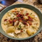 A close-up of a bowl of creamy New England clam chowder, topped with crispy bacon and fresh parsley.