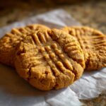 Close-up of three classic peanut butter cookies with distinctive fork marks, resting on parchment paper.