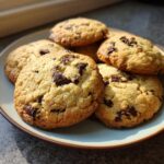 A close-up, overhead shot of a plate filled with warm, golden-brown chocolate chip cookies.