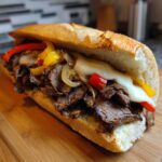 Close-up of an authentic Philly cheesesteak sandwich overflowing with thinly sliced steak, melted cheese, and sautéed peppers and onions.