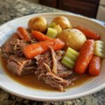 A comforting bowl of pot roast with tender shredded beef, carrots, potatoes, and celery in a rich gravy.