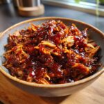 A bowl filled with tender, shredded pulled pork covered in a rich, glossy BBQ sauce.