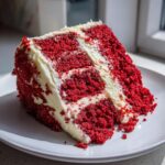 A decadent slice of red velvet cake with creamy white frosting, showcasing its rich red layers.