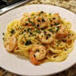 A close-up of a white plate filled with linguine pasta topped with succulent shrimp scampi and fresh parsley.