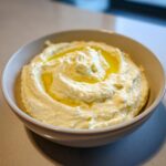 A bowl of smooth, creamy hummus drizzled with golden olive oil, ready to be served.