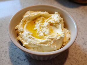 A small white bowl filled with creamy hummus, topped with a generous drizzle of golden olive oil.