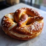 Close-up of a perfectly baked soft pretzel, glistening with coarse salt crystals.
