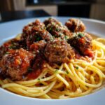 A close-up of a white plate filled with spaghetti and meatballs in marinara sauce, topped with parsley and parmesan.