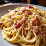 Close-up of a plate of authentic spaghetti carbonara, coated in creamy sauce and topped with crispy guanciale and black pepper.