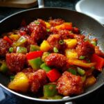 Close-up of crispy sweet and sour chicken with bell peppers and pineapple in a pan.