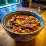 A close-up of a steaming bowl of taco soup, filled with ground beef, kidney beans, corn, and tomatoes.
