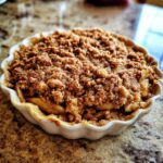 A close-up of a warm apple crisp in a white ramekin, topped with a golden-brown crumble.