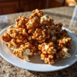 A white plate piled high with glossy, homemade caramel popcorn crunch, glistening in the sunlight.
