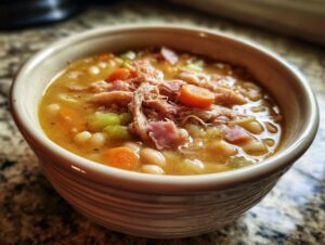 Close-up of a hearty bowl of amazing ham and bean soup, featuring shredded ham, white beans, carrots, and celery.