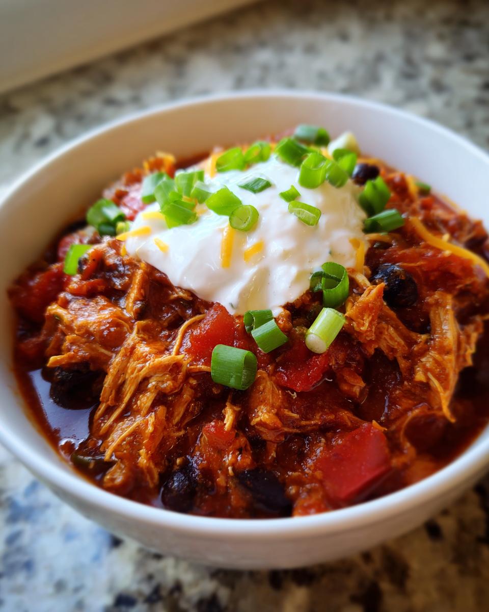 Close-up of a hearty bowl of shredded Turkey chili topped with a dollop of sour cream and sliced green onions.
