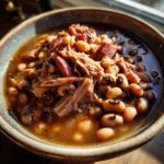 Close-up of a bowl of hearty black-eyed peas with tender shredded smoked meat and savory broth.