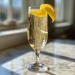 A bubbly French 75 cocktail served in a tall champagne flute, garnished with a lemon twist.