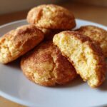 A close-up of several chewy snickerdoodle cookies, one broken in half, on a light gray plate.