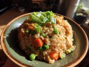 A close-up of a bowl of homemade chicken fried rice, featuring rice, peas, carrots, egg, and green onions.
