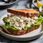 A delicious chicken salad sandwich on toasted bread with crisp lettuce and visible chunks of chicken and celery.