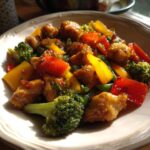 A close-up of a vibrant chicken stir fry featuring tender chicken pieces, broccoli florets, red and yellow bell peppers, and green beans in a glossy sauce.