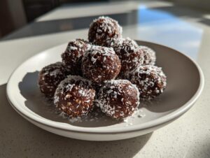 A stack of dark chocolate rum balls rolled in shredded coconut, presented on a light gray plate.