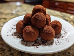 A pile of rich chocolate truffles generously dusted with cocoa powder on a white plate.