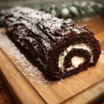 A slice of a rich chocolate Yule log cake filled with cream and dusted with powdered sugar.
