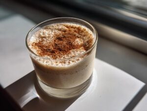 A glass of creamy Coquito topped with a generous dusting of cinnamon, catching the sunlight.