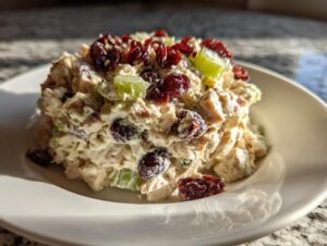 A mound of creamy turkey salad mixed with celery and topped with dried cranberries, served on a white plate.