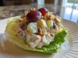 A scoop of creamy Waldorf salad, featuring apples, grapes, and walnuts, served in a crisp lettuce cup.