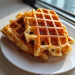 Close-up of two golden-brown, crispy and fluffy waffles stacked on a white plate.