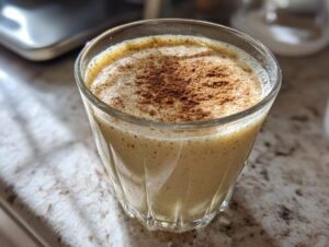 A close-up of a glass of creamy eggnog, dusted with cinnamon.
