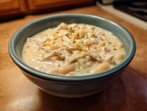 A close-up of a bowl of creamy White Chicken Chili topped with shredded chicken, white beans, and shredded cheese.