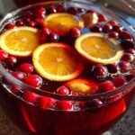 Close-up of a vibrant red holiday punch garnished with floating orange slices and fresh cranberries.
