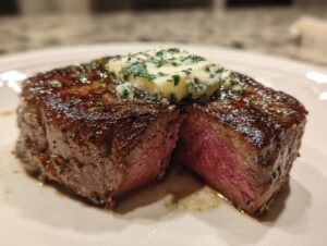 Close-up of a medium-rare filet mignon steak, sliced open, topped with melting herb butter.
