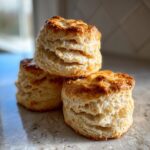 A stack of three golden-brown, flaky buttermilk biscuits with visible layers.
