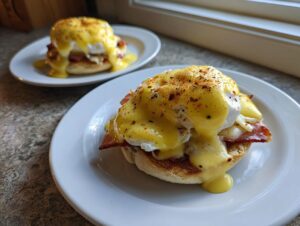 Two plates of classic Eggs Benedict topped with rich hollandaise sauce and paprika.