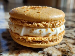 Close-up of a golden brown macaron with a creamy white filling and a dusting of cinnamon.