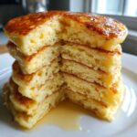 Close-up of a tall stack of fluffy buttermilk pancakes cut in half, showing the airy interior and dripping syrup.