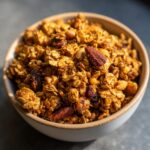 Close-up of a bowl filled with golden, crunchy granola featuring nuts and dried fruit.