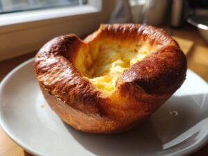 A single, perfectly risen Yorkshire pudding with a deep golden-brown, crispy exterior, sitting on a white plate.