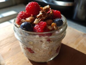 Close-up of a jar filled with overnight oats, topped with fresh raspberries, blueberries, and walnuts.