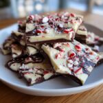 A close-up of a stack of homemade peppermint bark, featuring dark and white chocolate swirled and topped with crushed candy canes.
