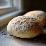 Two golden-brown balls of fresh pizza dough dusted with flour, resting on a cooling rack.