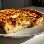 A delicious slice of Quiche Lorraine on a plate, showcasing its rich custard and crispy bacon.