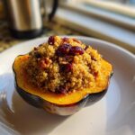A roasted half of stuffed acorn squash filled with golden quinoa, dried cranberries, and pecans.
