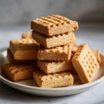 A close-up stack of golden brown shortbread cookies with a classic dimpled pattern on top.